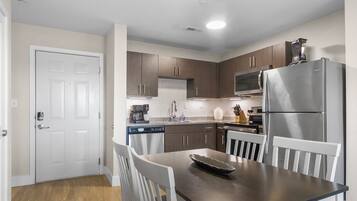 A modern kitchen with wooden cabinets, a stainless steel refrigerator, and a dining table with white chairs.