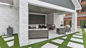 Patio esterno con mobili in vimini, ventilatore a soffitto ed erba sintetica.