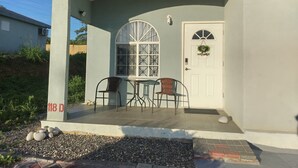 Una casa con un portico, una porta bianca con un cartello di benvenuto, due sedie e un tavolo.