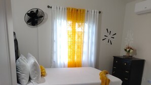 Una camera da letto con un letto, un comodino, una cassettiera, una ventola e una finestra con tende.
