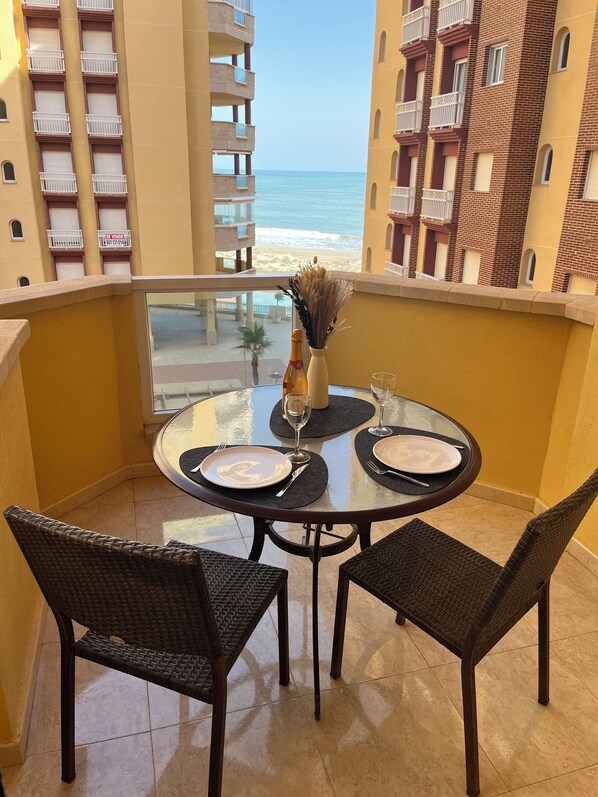 A balcony with a table set for two, overlooking a beach and high-rise buildings. - Playa Príncipe, direct beach access in La Manga del Mar Menor (La Manga del Mar Menor)
