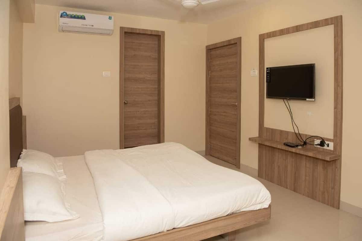 Quarto com cama, guarda-roupa de madeira, televisão na parede e ar condicionado.