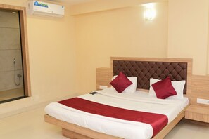 Une chambre d’hôtel avec un lit, une tête de lit en bois, un plaid rouge et une douche intégrée.