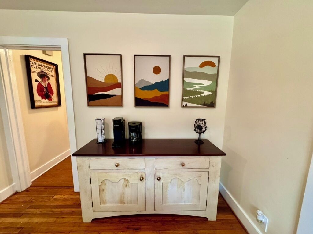 A wooden cabinet with two drawers and a shelf, placed against a wall with three framed artworks above it.