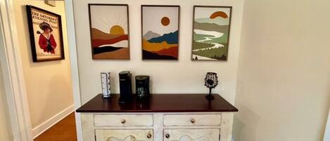 A wooden cabinet with two drawers and a shelf, placed against a wall with three framed artworks above it.