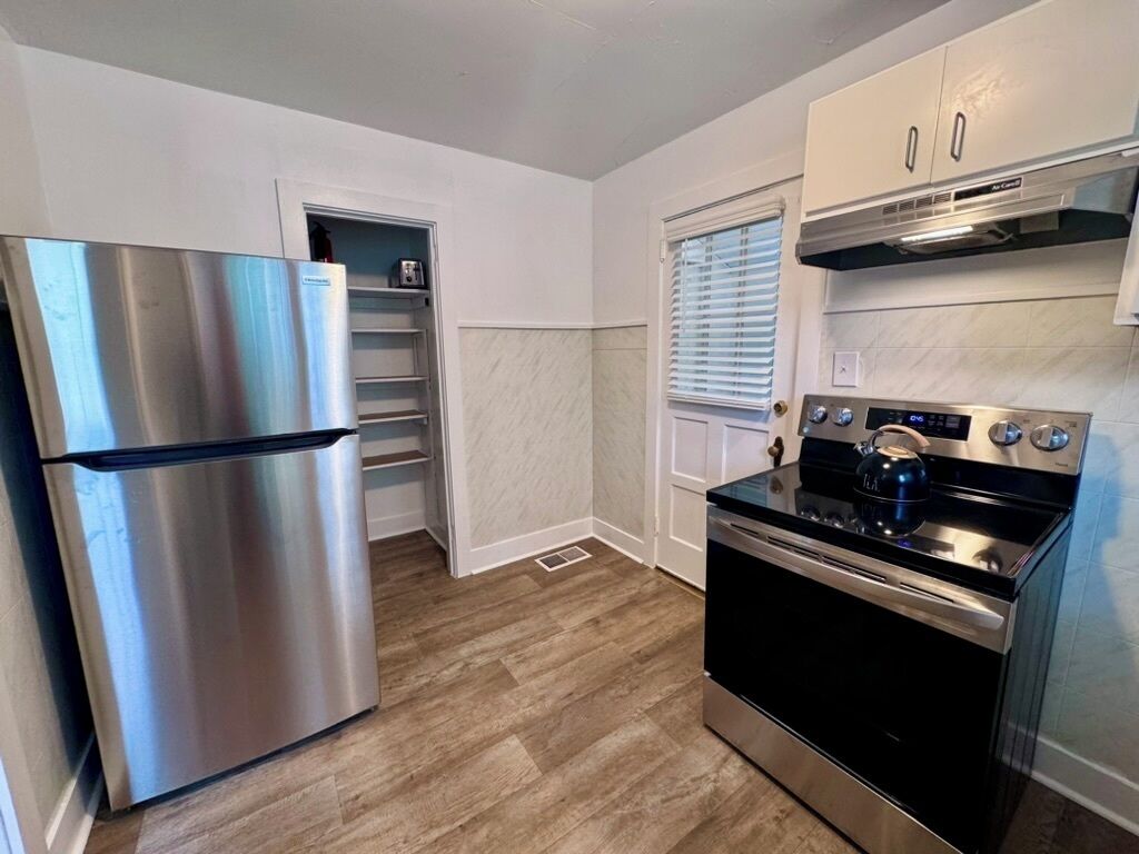 A compact kitchen with a stainless steel refrigerator, a black stove, and white cabinets.