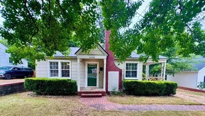A two-story house with a brick chimney, a front porch, and a well-maintained lawn. - Tea Olive Cottage - 2BR Near Augusta National, Downtown & Medical District (Augusta)