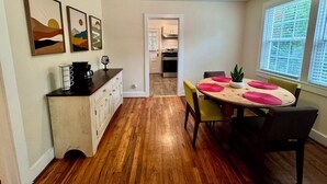 A dining area with a wooden table, chairs, and artwork on the wall. - Tea Olive Cottage - 2BR Near Augusta National, Downtown & Medical District (Augusta)