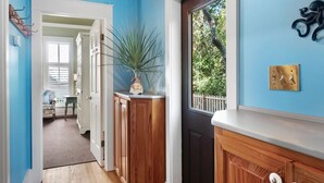 Un couloir avec une armoire en bois, une plante en pot et une porte donnant sur une fenêtre.