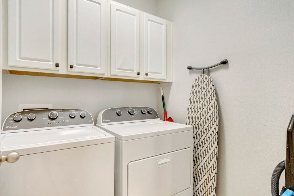 Una sala de bugaderia amb dues rentadores i assecadores Whirlpool blanques, un tintxador metàl·lic i una tovallola amb dibuixos penjada a un ganxo.