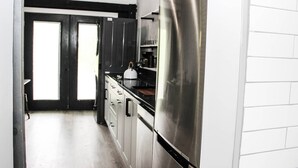 A modern kitchen with stainless steel appliances, black cabinets, and a view of the outside through a large window. - Hits | Catskills Views | Pet Friendly | Studio (Saugerties)