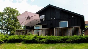 A black house with a wooden deck, an air conditioning unit, and a large umbrella. - Hits | Catskills Views | Pet Friendly | Studio (Saugerties)