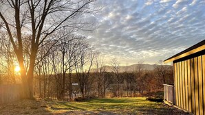 A gravel driveway leading to a wooden building with a metal fence, surrounded by trees and a view of distant mountains. - Hits | Catskills Views | Pet Friendly | Studio (Saugerties)