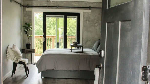 A bedroom with a bed, a chair, a small table, and a ceiling fan. - Hits | Catskills Views | Pet Friendly | Studio (Saugerties)