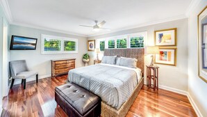 A bedroom with a large bed, a ceiling fan, a chair, a nightstand, and framed pictures on the wall.
