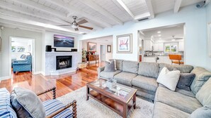A spacious living room with a fireplace, a large sofa, a coffee table, and a dining area in the background.