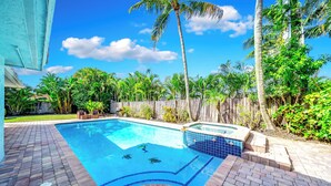 A swimming pool with a hot tub, surrounded by palm trees and a wooden fence.