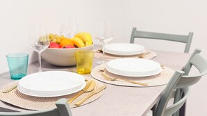 A dining table set with white plates, gold cutlery, and a bowl of fruit.