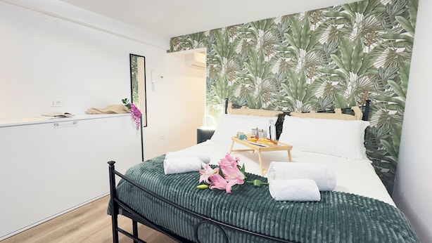 A modern bedroom with a bed, a bedside table with a tray of breakfast, a mirror, and a tropical leaf-patterned wall.