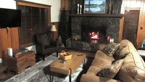 Ein gemütliches Wohnzimmer mit Kamin aus Stein, einer bequemen Couch, einem Couchtisch und einem an der Wand befestigten Fernseher.