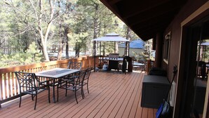 Eine Holzterrasse mit Tisch, Stühlen, einem Grill und einem überdachten Sitzbereich.