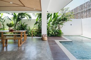 An outdoor pool area with a wooden deck, a concrete floor, and lush tropical plants. - Traditional/modern 3-story villa w/ ocean views (Kecamatan Kuta Selatan)