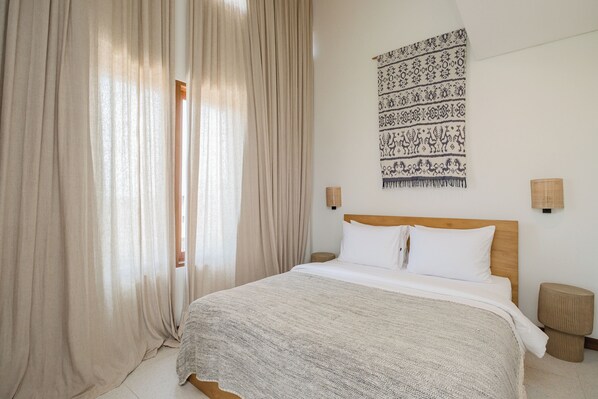A bedroom with a large bed, beige curtains, a patterned tapestry, and two wall-mounted lamps. - Traditional/modern 3-story villa w/ ocean views (Kecamatan Kuta Selatan)