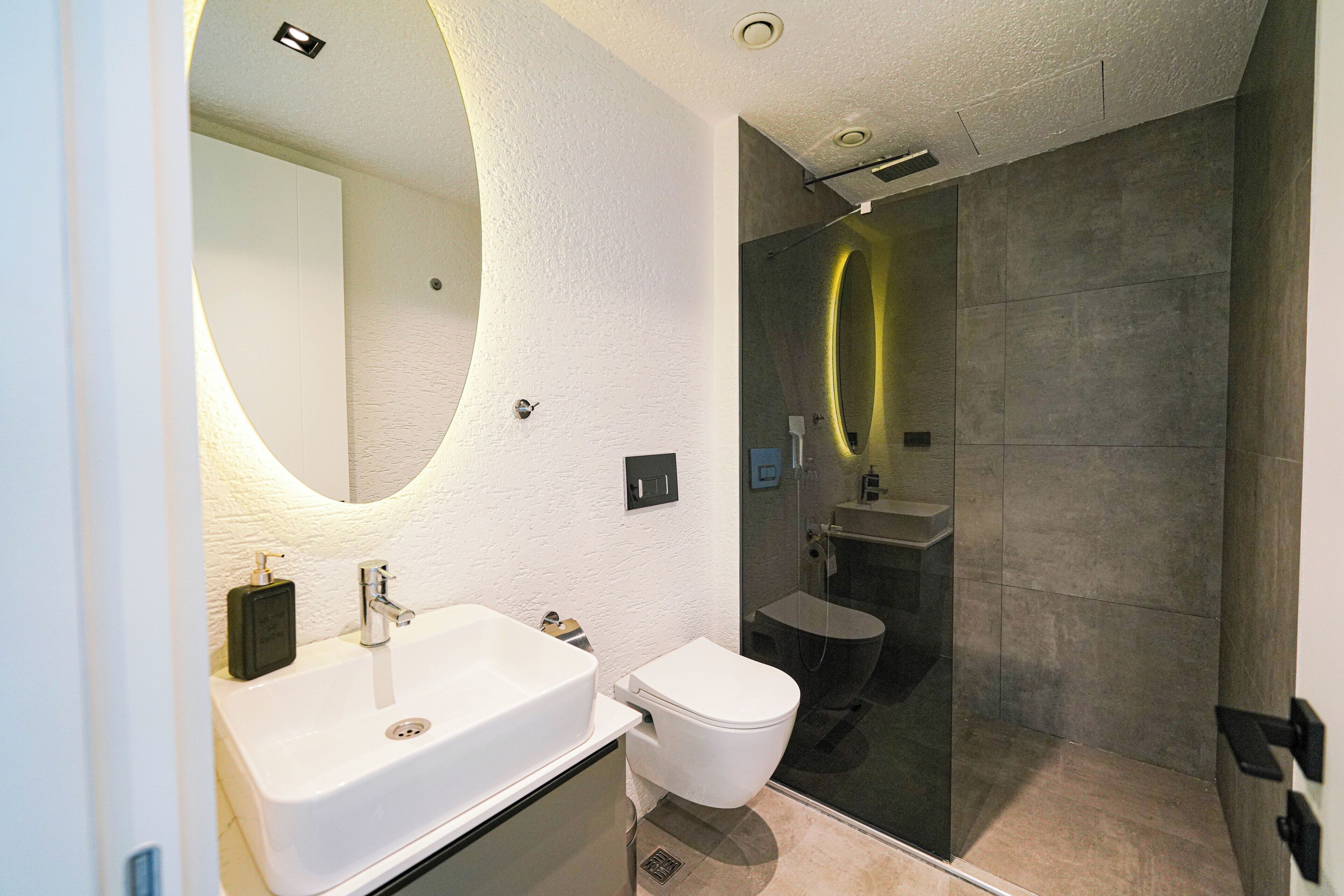 Un baño moderno con un lavamanos blanco, un inodoro y una zona de ducha con mampara de vidrio.