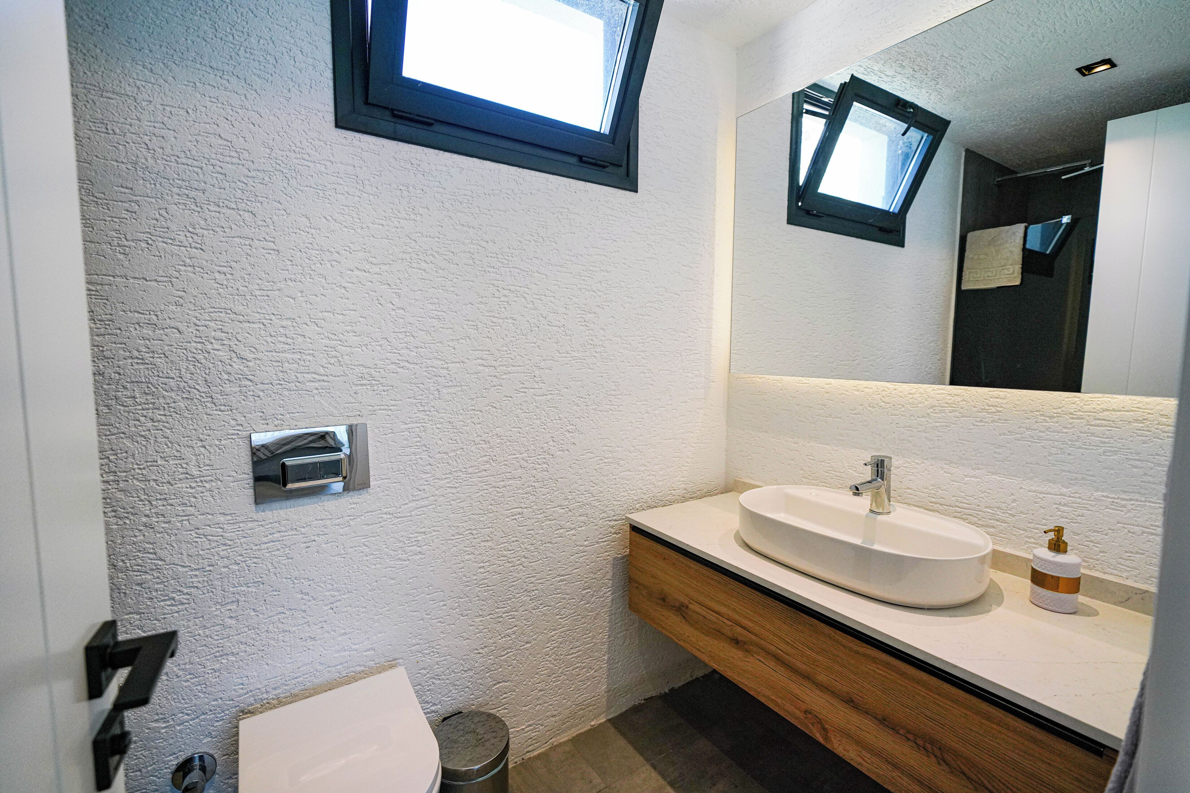 Een moderne badkamer met een lichtgekleurde wand, een houten wastafelmeubel, een witte wasbak en een spiegel boven het meubel.