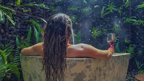 Eine Person entspannt in einer Steinschaukelbadewanne, umgeben von üppigem Grün.