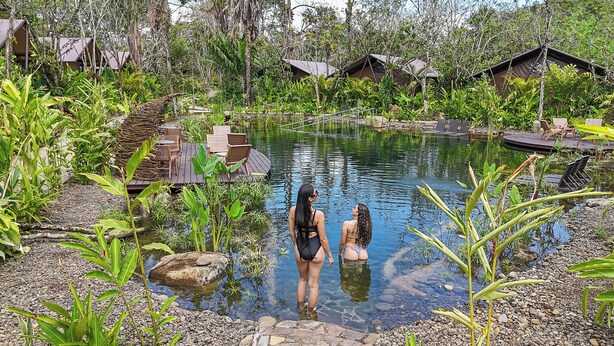 Ein natürlicher Pool, umgeben von üppiger Vegetation und Holzkonstruktionen.