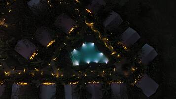 A geometric structure with illuminated edges and a central glowing area, surrounded by foliage.