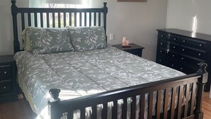 Une chambre à coucher avec un lit en bois, une table de chevet, une commode, une fenêtre avec des rideaux et un luminaire au plafond.