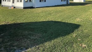 Une maison blanche d’un seul étage, dotée d’une grande véranda à l’avant et d’un petit garage attenant.