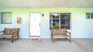 A covered porch with two wooden benches, a white door with the number 3, and a window with a view of palm trees. - Beach Unit! Walk To Beach & Restaurants / Shops! (Pompano Beach)