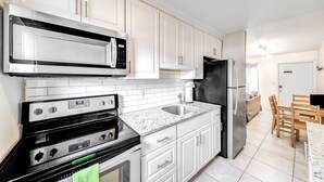 A modern kitchen with white cabinets, a stainless steel refrigerator, a microwave, and a stove. - Beach Unit! Walk To Beach & Restaurants / Shops! (Pompano Beach)