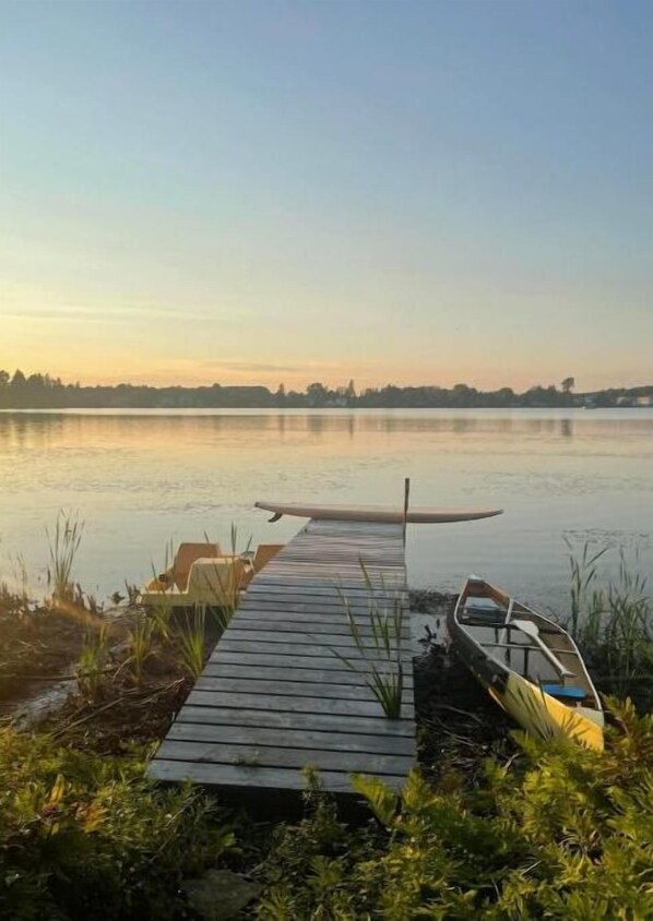 Une jetée en bois s’étendant sur un lac paisible, avec un bateau et une planche de surf qui s’y trouvent.