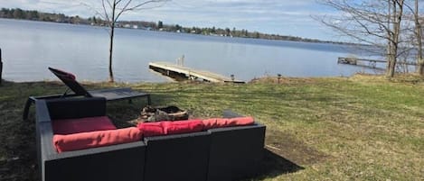 A black outdoor seating area with red cushions, a wooden dock, and a lake view.