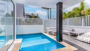 Ein Poolbereich mit Glasveranda, weißer Gartenmöbel und Blick auf Palmen.