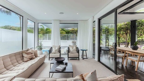 Ein modernes Wohnzimmer mit Sofa, Couchtisch und Sesseln, großen Fenstern und Blick ins Freie.