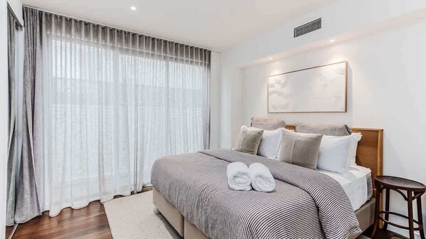A hotel room with a bed, a bedside table, a window with curtains, and a wall-mounted artwork.