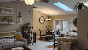 A living room with a ceiling fan, a dining area with a chandelier, and a kitchen visible through an open door.