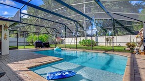 A covered swimming pool with a blue inflatable float, surrounded by a brick deck and a white fence.