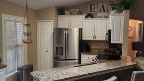 A kitchen with white cabinets, a stainless steel refrigerator, a granite countertop, and a hanging light fixture.