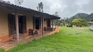 A building with a porch, a staircase, and a grassy yard. - Pousada das Flores (Gonçalves)