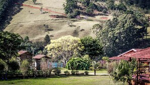 A rural landscape with a hill, scattered trees, and a few buildings with red roofs. - Pousada das Flores (Gonçalves)
