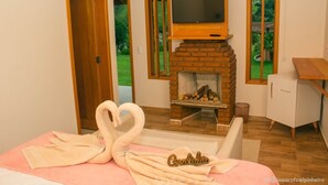 A room with a fireplace, a television, and a bed with towels arranged in a swan shape. - Pousada das Flores (Gonçalves)