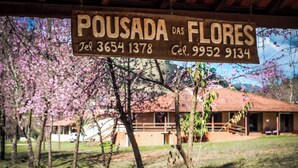 A wooden sign with the text "POUSADA DAS FLORES" and contact numbers. - Pousada das Flores (Gonçalves)