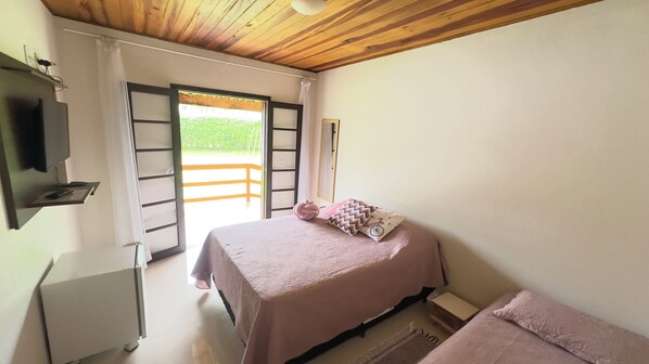 A bedroom with a bed, a TV mounted on the wall, a window with a view of greenery, and a wooden ceiling. - Pousada das Flores (Gonçalves)