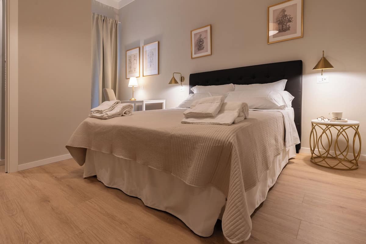 A neatly made bed with white linens, a bedside table with a lamp, and a framed picture on the wall.